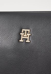 Surface en cuir noir texturé avec un petit logo métallique doré représentant les lettres entrelacées T et H.