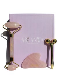 Rouleau de jade en quartz rose et outil gua sha sur une boîte violette claire, avec des accents dorés et un relief, texture lisse et formes arrondies.
