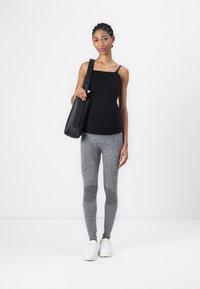 Top nero senza maniche, leggings grigi a trama e sneakers bianche. La modella tiene una borsa a spalla nera. Design semplice con finiture lisce.