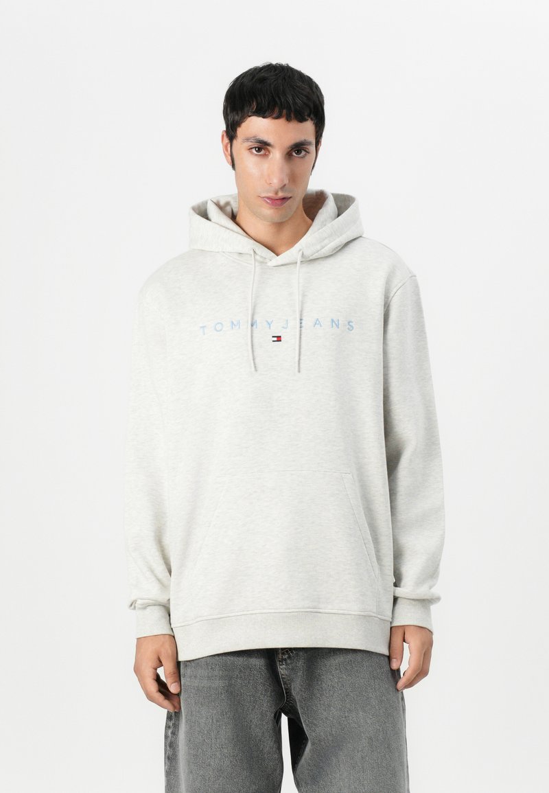 Grå hettegenser laget av mykt stoff med en frontlomme og justerbar snøring. Har "TOMMY JEANS" i lyseblå tekst over brystet.