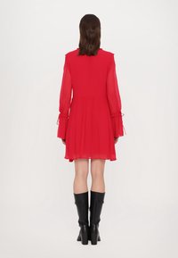 Rode chiffon jurk met lange klokmouwen, gegatherde taille en een vloeiende rok. Draag het met kniehoge zwarte laarzen.