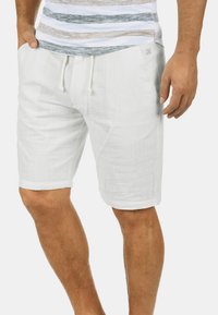 Shorts en lin blanc avec un taille élastique, des poches latérales et une coupe décontractée ; le tissu texturé apporte une sensation de légèreté.