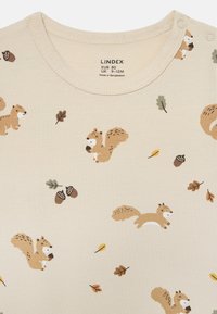 Beige Baumwollhemd mit verspielten Mustern von Eichhörnchen und Eicheln sowie grünen und braunen Blättern. Druckknöpfe an der Schulter für ein einfaches Ankleiden.