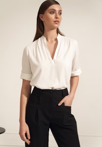 Biała bluzka z kołnierzykiem i podwiniętymi rękawami, zestawiona z czarnymi spodniami o wysokim stanie z bocznymi kieszeniami i zapięciem na guzik. Prosty design.