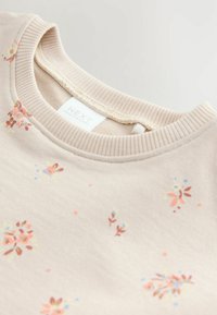 Indumento beige chiaro con piccole stampe floreali rosa e blu e scollo rotondo a coste, con etichetta interna del marchio "Next".