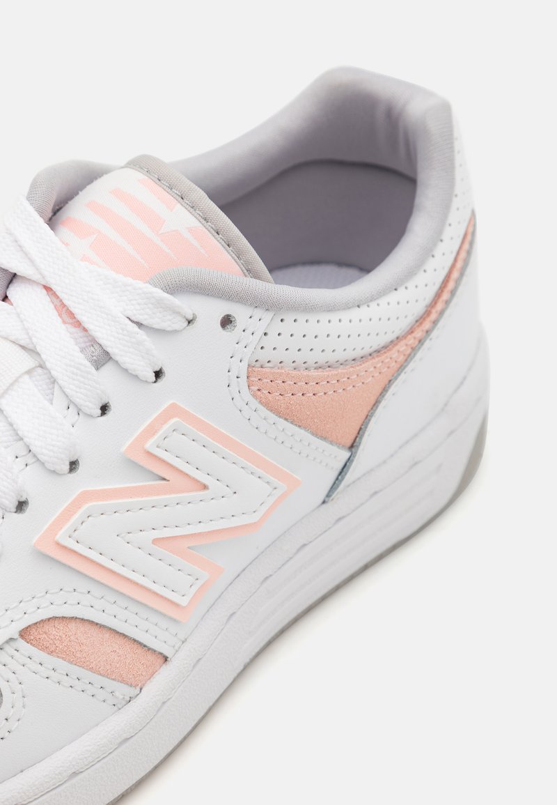 Weiße Sneakers mit rosa und grauen Akzenten, ausgestattet mit perforierten Details, Schnürverschluss und einer strukturierten Sohle. Markenlogo gut sichtbar.