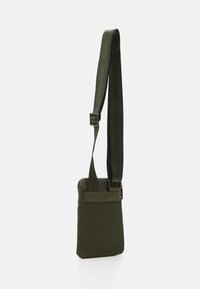 Borsa a tracolla verde oliva con chiusura a zip e tracolla regolabile. Realizzata in tessuto resistente, presenta una tasca frontale con flap in velcro.