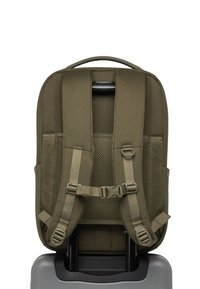 Maslinasto zelena torba na leđa s podstavljenim trakama i mrežastim detaljima, pričvršćena za ručku sive koferke, s robusnim dizajnom i sigurnim kopčama.