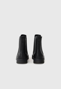Botas de tobillo de cuero negro con un acabado texturizado, paneles laterales elásticos y un diseño elegante con una suela de goma baja.
