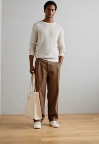 Pull en tricot crème, pantalon à jambes larges marron, baskets blanches et sac fourre-tout beige. Le tissu est texturé et les couleurs sont neutres.