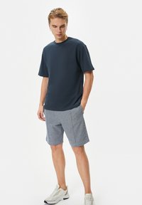T-paita tummansinistä puuvillaa, jossa on lyhyet hihat, yhdistetty vaaleanharmaisiin kuvioituihin shortseihin. Mallilla on päällään vaaleat sneakerit. Yksinkertainen, rento asu.