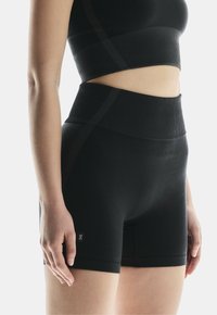 Schwarze Sportshorts mit hohem Bund, gerippter Textur und kleinem Logo an der Seite. Glattes Material, das für Dehnbarkeit und Komfort ausgelegt ist.