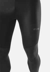 Collant compressivi neri con una finitura liscia, dotati di un pannello texturizzato sulla parte inferiore della gamba e un logo bianco discreto sulla coscia.