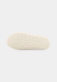 Πάτος ενός λευκού παπουτσιού με γεωμετρικό τριγωνικό μοτίβο που παρέχει υφή για καλύτερο κράτημα, εμφανιζόμενος επίπεδος πάνω σε ουδέτερο φόντο.