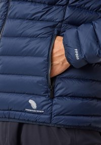 Marineblauwe pufferjack met een gequilt ontwerp, voorzien van een ritszak en het logo "Premium Down". Het materiaal is soepel met een lichte glans.