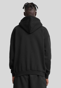 Felpa nera con cappuccio a coulisse, spalle scese e polsini e orlo ribattuti. Tessuto soffice con vestibilità rilassata. Nessun motivo visibile.