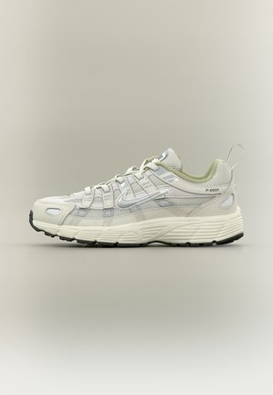 Lichtgrijze en witte sportschoen met mesh panelen, vetersluiting, Nike-logo en zwarte rubberen zool, zijaanzicht.