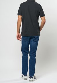 Svart pikétröja med kort ärm, kombinerad med blå denimjeans. Jeansen har en klassisk passform med bakfickor och vita sneakers.