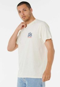 Kremowa bawełniana koszulka z krótkim rękawem i okrągłym dekoltem. Na lewej piersi znajduje się niebiesko-pomarańczowe logo "Rip Curl Surfboards".