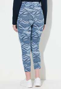 Blå mönstrade leggings har en design med vågor och djurtextur. Tyget är stretchigt och åtsittande, slutande precis ovanför fotleden.