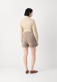 Beige long-sleeve shirt paired with brown and cream patterned high-waisted shorts, worn with brown flat shoes. Simple, clean design.