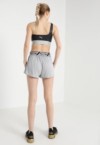 Svart sportbh med silverdetaljer, grå shorts med svart elastisk midja. Modellen bär svarta sneakers med texturerade sulor.