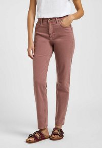 Jeans de corte ceñido y talle alto en rosa empolvado, con diseño clásico de cinco bolsillos y detalles de costura sutiles, combinados con sandalias de tiras.