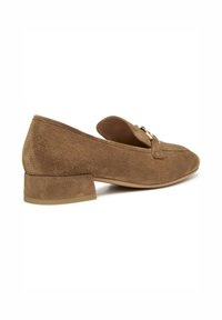 Zapatos de ante marrón sin cordones con un bajo tacón cuadrado, que presentan una tira decorativa y un detalle de hebilla en la punta. Textura suave, forma redondeada.