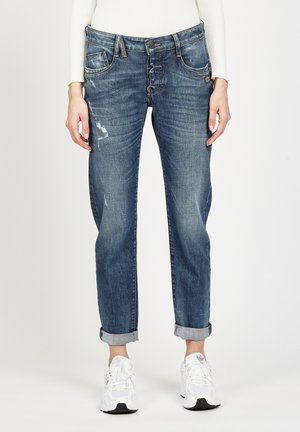 Dark blue jeans with a relaxed fit, featuring a distressed design, rolled cuffs, and light fading. Worn with white sneakers.