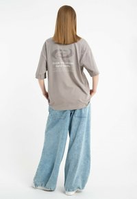 Szara, oversize'owa koszulka z krótkim rękawem, z grafiką tekstową na plecach, oraz luźne, jasnoniebieskie dżinsowe spodnie z szerokimi nogawkami i kieszeniami.