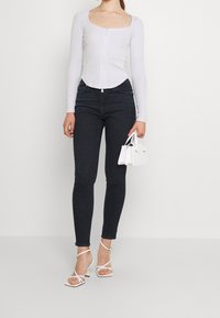 Maglietta lunga grigia chiara con texture a coste e scollatura quadrata, abbinata a jeans skinny scuri e tacchi a strappo bianchi. Inclusa una borsa bianca.