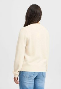 Maglione color crema con colletto rotondo e polsini a coste. Tessuto morbido, spalle scese e vestibilità comoda, abbinato a jeans blu.