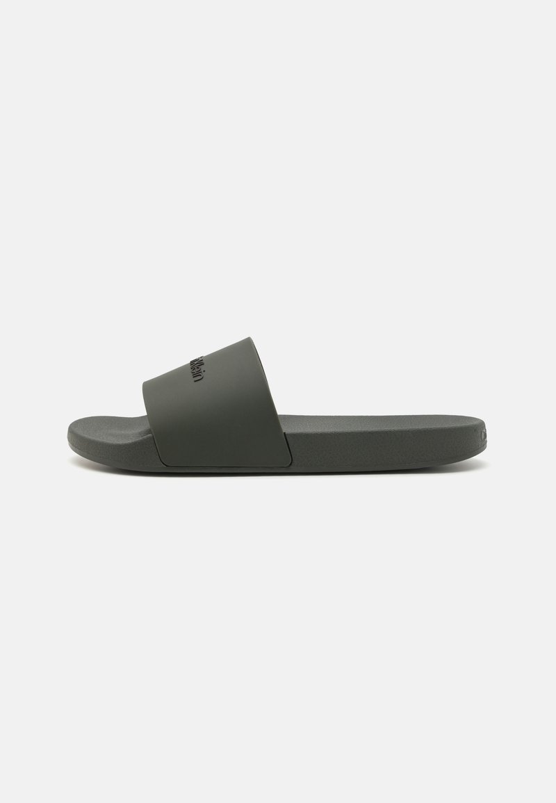 Donkergroene schuifsandalen van matte rubber met een brede band en een gestructureerde voetbed. Voorzien van minimalistische merkaccenten in reliëflettertype.