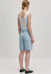 Lichtblauwe denimshorts met een hoge taille, voorzien van twee achterzakken en een relaxte pasvorm, gecombineerd met een witte mouwloze top.