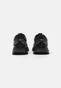 Zwarte sportieve schoenen met een gestructureerde mesh bovenkant, contrasterende gouden accenten, een dikke zwarte zool en versterkte hielriemen.