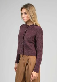 Cardigan court bourgogne foncé en mélange de laine douce avec col rond, fermeture à boutons sur le devant et finition texturée. Associé à un pantalon couleur tan taille haute.