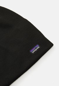 Berretto lavorato a maglia nero con finitura testurizzata e un piccolo etichetta rettangolare del logo Patagonia con grafica di montagne blu e rosse.