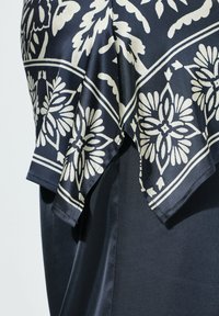 Falda de satén negra con una bufanda de patrón floral en azul marino y blanco drapeada sobre la cintura, mostrando la textura y los pliegues de la tela.