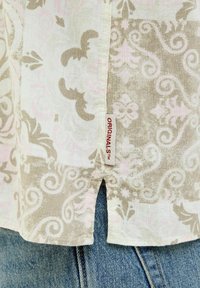 Camisa de tela ligera con un patrón de paisley en beige y rosa claro, con una pequeña etiqueta roja de "ORIGINALS" en la costura lateral.