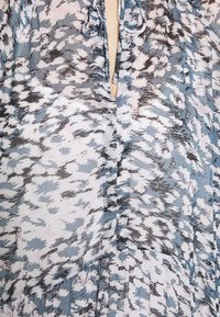 Květinová blůza v světle modré, tmavě modré a černé barvě. Má výstřih do V, detaily se šněrováním a jemnou texturu s pružným designem.