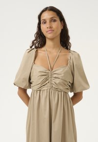 Robe beige avec des manches bouffantes et un corsage froncé, dotée de fines bretelles et d'une jupe fluide. Texture de tissu lisse, accents de design minimaux.
