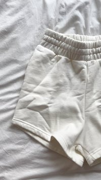Bermudas blancas de algodón con una cinturilla elástica fruncida, textura suave y piernas cortas; sin patrones visibles ni detalles de hardware.