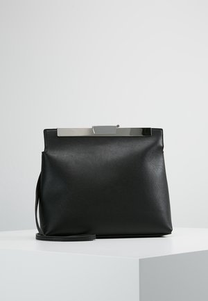 Schwarze Lederhandtasche mit strukturierter Form, die einen metallischen Verschluss oben und einen abnehmbaren Riemen für vielseitiges Tragen aufweist.