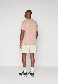 Beige bomulls-t-shirt med kort ärm, kombinerad med ljusa cargoshorts och svarta sportskor med vita detaljer och strumpor.