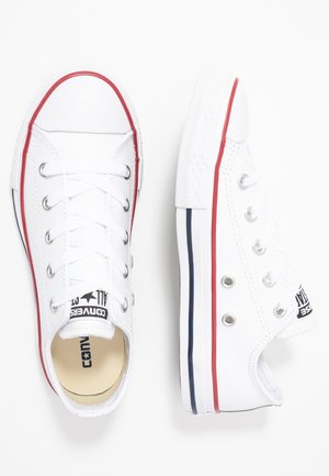 Paire de baskets basses blanches avec des rayures rouges et bleues sur la semelle et des œillets métalliques pour les lacets sur fond blanc.