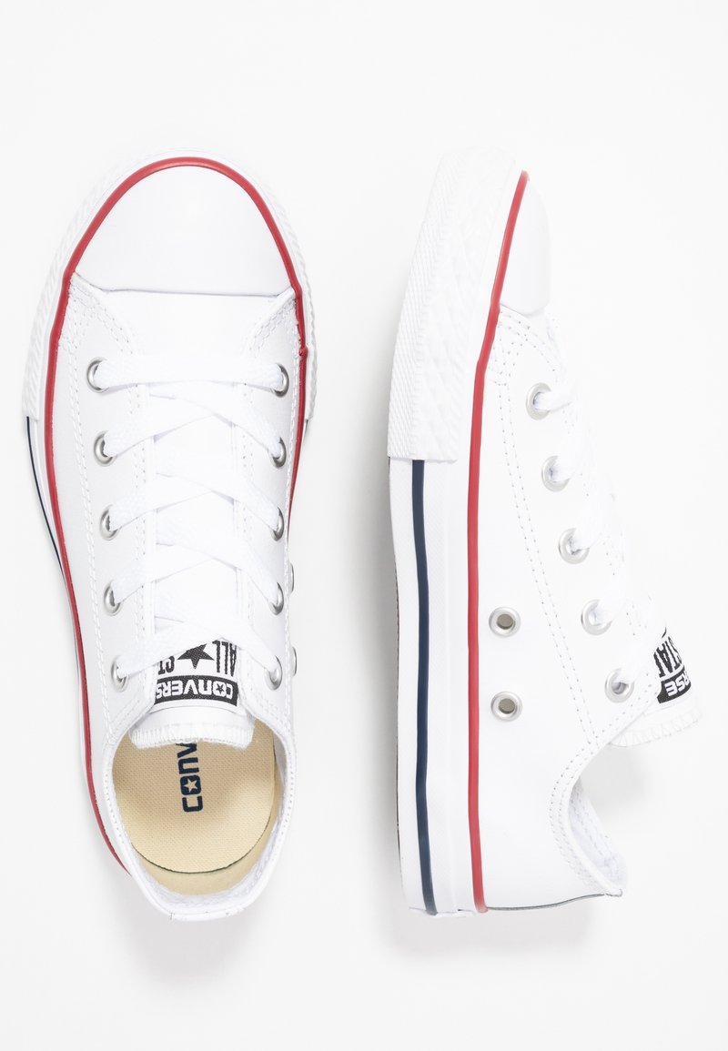 Paire de baskets basses blanches avec des rayures rouges et bleues sur la semelle et des œillets métalliques pour les lacets sur fond blanc.