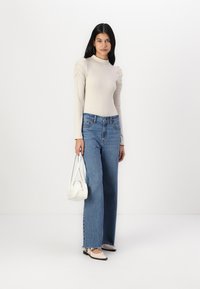 Bluza bej cu mânecă lungă și umeri bombat, asortată cu blugi evazați de culoare albastru deschis și balerini crem. Poșetă albă ca accesoriu.