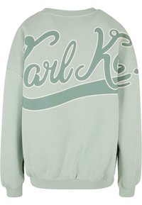Sweat-shirt vert clair avec un grand texte cursif "Karl K." et une bande ondulée à l'arrière, avec des poignets et un ourlet côtelés.