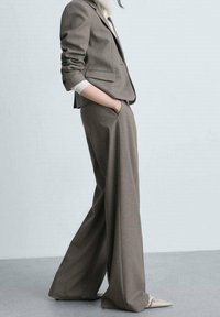 Harmaat räätälöidyt puku, jossa on istuva blazer ja leveälahkeiset housut, valmistettu teksturoidusta kankaasta. Valkoinen paita alla ja kärkitossut beigen värisinä.