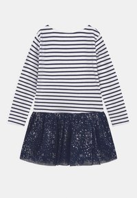 Långärmad klänning med vita och marinblå ränder på överdelen; marinblå utsvängd kjol med metalliska prickar, flödande tulletyg, rundad halsringning.